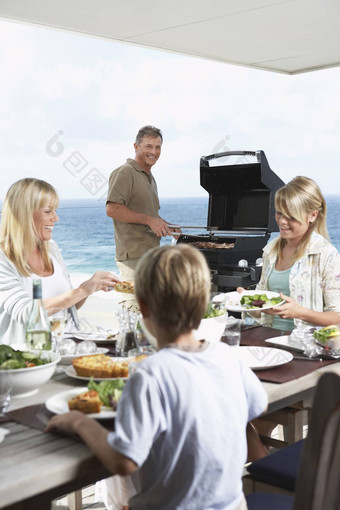 家庭坐着表格吃烧烤食物父亲站烧烤烧烤