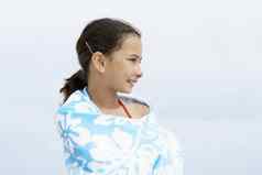 快乐青春期前的女孩包装毛巾站海滩