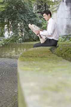 一边视图年轻的商人阅读报纸墙公园