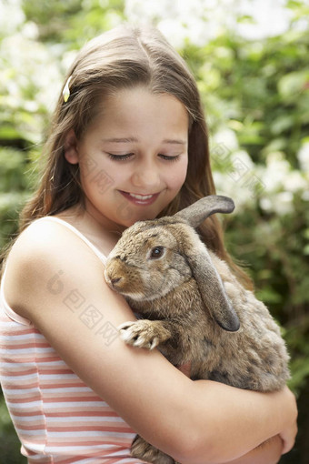 快乐年轻的女孩持有兔子兔子后院
