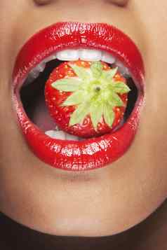 诱人的女人红色的嘴唇吃草莓