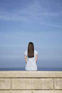 后视图年轻的女人坐着石头窗台海滩