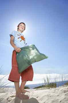 低角肖像年轻的男孩携带塑料袋填满垃圾海滩