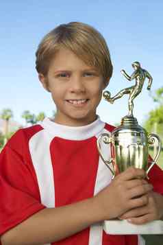 肖像年轻的男孩持有足球奖杯骄傲
