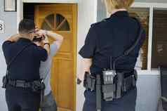 后视图警察军官逮捕年轻的男人。房子