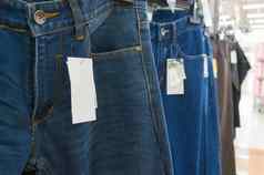 空白白色标签蓝色的牛仔裤悬挂器架子上超级市场
