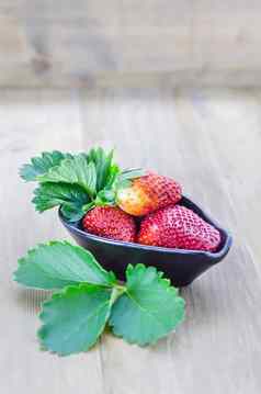 新鲜的草莓水果黑色的碗绿色叶子木背景