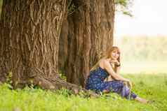 美丽的年轻的女人坐根大树看起来如痴如梦