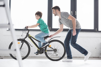 一边视图年轻的父亲帮助儿子骑自行车