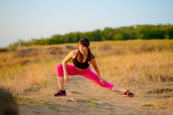 年轻的健身女人伸展运动野生公园女跑步者延伸健康的生活方式概念