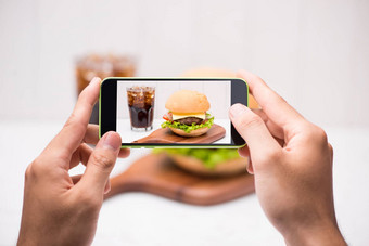 手持有智能手机采取照片自制的烧烤汉堡