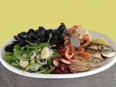 孤立的海鲜盘新鲜的混合烤贻贝小龙虾虾鱼装饰芝麻菜洋葱柠檬酱汁白色板