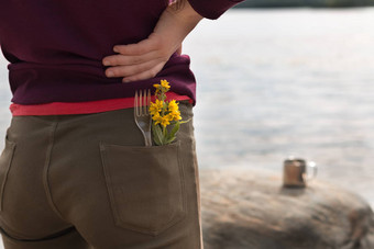 英俊的女旅游穿棕色（的）牛仔裤紫色的运动衫叉黄色的花口袋里站河银行享受视图山夏天徒步旅行旅行概念