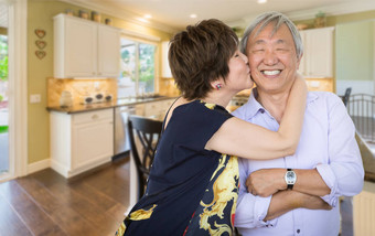 快乐高级中国人夫妇接吻内部美丽的自定义厨房