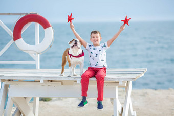 英俊的男孩青少年快乐支出时间朋友斗牛犬海一边孩子狗持有玩海星星关闭生活浮标浮动穿红色的裤子裤子拖鞋t恤