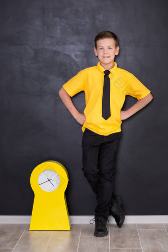 可爱的英俊的学校男孩黄色的t恤领带时尚的靴子casuals站关闭黑色的董事会黄色的时钟看微笑