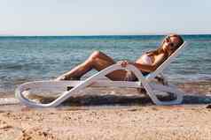 年轻的女人泳衣穿太阳镜谎言帆布躺椅