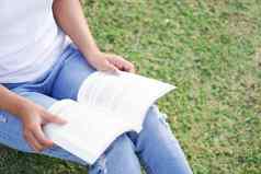 特写镜头年轻的女人阅读书坐着绿色草