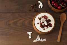 燕麦片酸奶水果樱桃葡萄干椰子芯片在一夜之间早餐健康的食物概念健身情绪饮食夏天光零食黑暗木背景