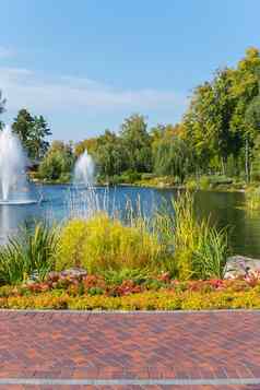 美丽的大池塘郁郁葱葱的喷泉包围高绿色树花床花蓝色的清晰的天空坟墓