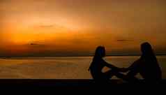 轮廓漂亮的女孩坐持有手有趣的海边日落橙色天空夏天假期背包旅行概念