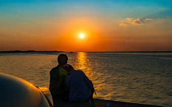 轮廓幸福夫妇坐着放松海滩前面车橙色蓝色的天空日落<strong>夏天</strong>假期旅行概念浪漫的年轻的夫妇<strong>约会</strong>海边