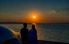 轮廓幸福夫妇坐着放松海滩前面车橙色蓝色的天空日落夏天假期旅行概念浪漫的年轻的夫妇约会海边