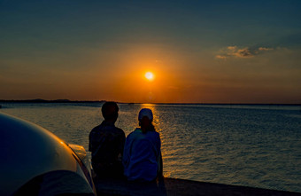 轮廓幸福夫妇坐着放松海滩前面车橙色蓝色的天空日落<strong>夏天</strong>假期旅行概念浪漫的年轻的夫妇<strong>约会</strong>海边