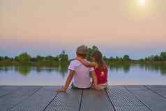 男孩平帽女孩坐着码头女孩拥抱老哥哥爱友谊童年概念美丽的浪漫的日落图片复制空间