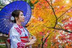 亚洲女人穿日本传统的和服伞秋天公园日本