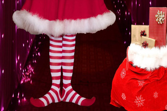 可爱的女孩穿红色的白色条纹精灵长袜可爱的衣服站圣诞老人老人袋完整的礼物背景圣诞节灯