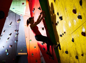年轻的活跃的女人抱石色彩斑斓的人工岩石攀爬健身房极端的体育运动室内攀爬概念
