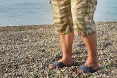 男人的脚人字拖短裤男人。站海滩卵石海滩日出早....