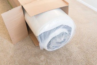 特写镜头前视图roll-packed春天床垫从箱子中取出地毯地板上背景