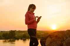 女人跑步者休息锻炼智能手机听音乐日落岩石体育概念