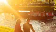 日落可爱的夫妇坐在银行河运河城市公园会谈运河浮点数快乐船好夏天周末