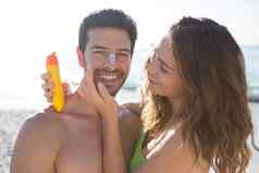 快乐女人应用sunscream微笑男人。脸海滩