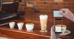 手拍摄杯卡布奇诺咖啡聪明的电话持有卡咖啡商店
