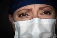 泪流满面的强调女医生护士穿医疗脸面具黑暗背景