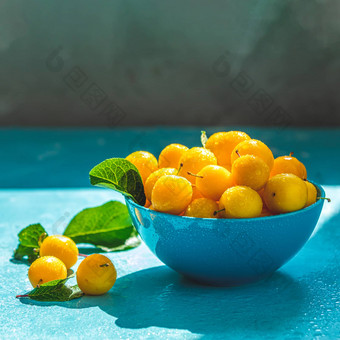 新鲜的甜蜜的黄色的樱桃李子水滴蓝色的碗