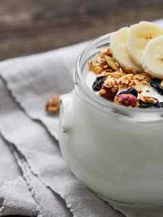 自然自制的酸奶玻璃Jar健康的食物早餐牛奶什锦早餐Jar格兰诺拉麦片香蕉片亚麻桌布木表格