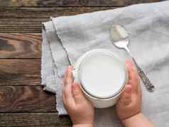自然自制的酸奶玻璃Jar健康的食物早餐孩子的手孩子持有Jar酸奶油亚麻桌布木表格