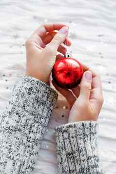 女人持有一年装饰闪闪发光的红色的圣诞节球白色织物背景银雪花