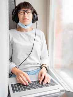 女人医疗面具远程作品首页坐在窗口窗台上移动PC膝盖耳机封锁检疫冠状病毒科维德隔离首页