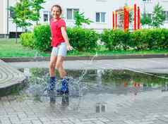 女孩蓝色的橡胶靴子跳水坑雨