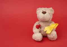 可爱的棕色（的）泰迪熊持有丝绸黄色的丝带形状