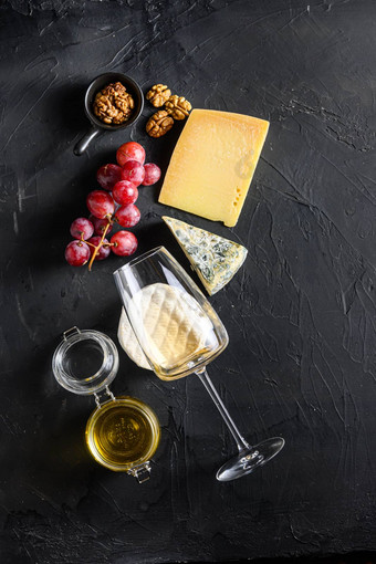 奶酪开胃菜选择抱怨零食集各种模具法国奶酪葡萄山核桃坚果白色长相思酒蜂蜜黑色的背景前视图复制空间垂直