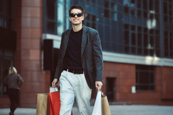 时尚的年轻的男人。太阳镜走城市街享受黑色的星期五购物时尚的商店城市