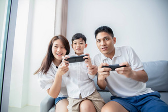 亚洲家庭有趣的玩电脑控制台游戏父亲儿子手机控制器妈妈。欢呼球员首页