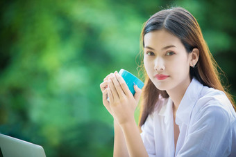 亚洲女人持有咖啡杯喝笔记本电脑工作首页早....